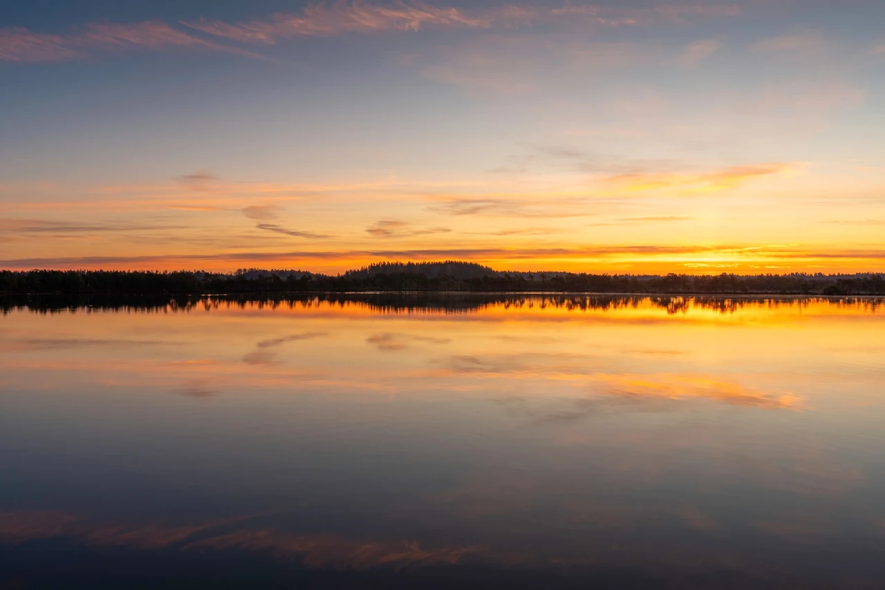 Mirror-still lake reflecting a soft dawn sky